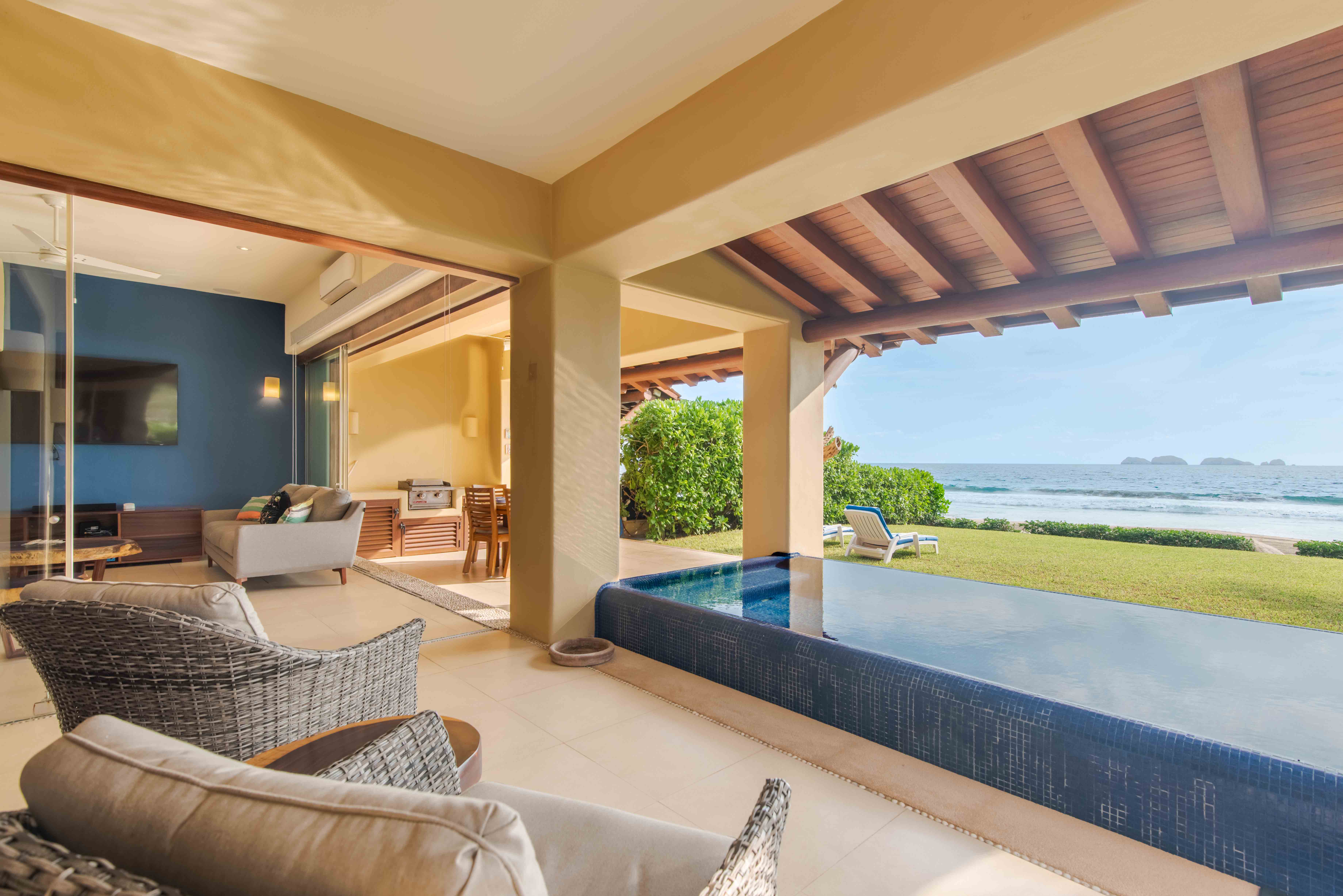 Architectural terrace with pool, lawn and Pacific Ocean views framed by rooflines and columns