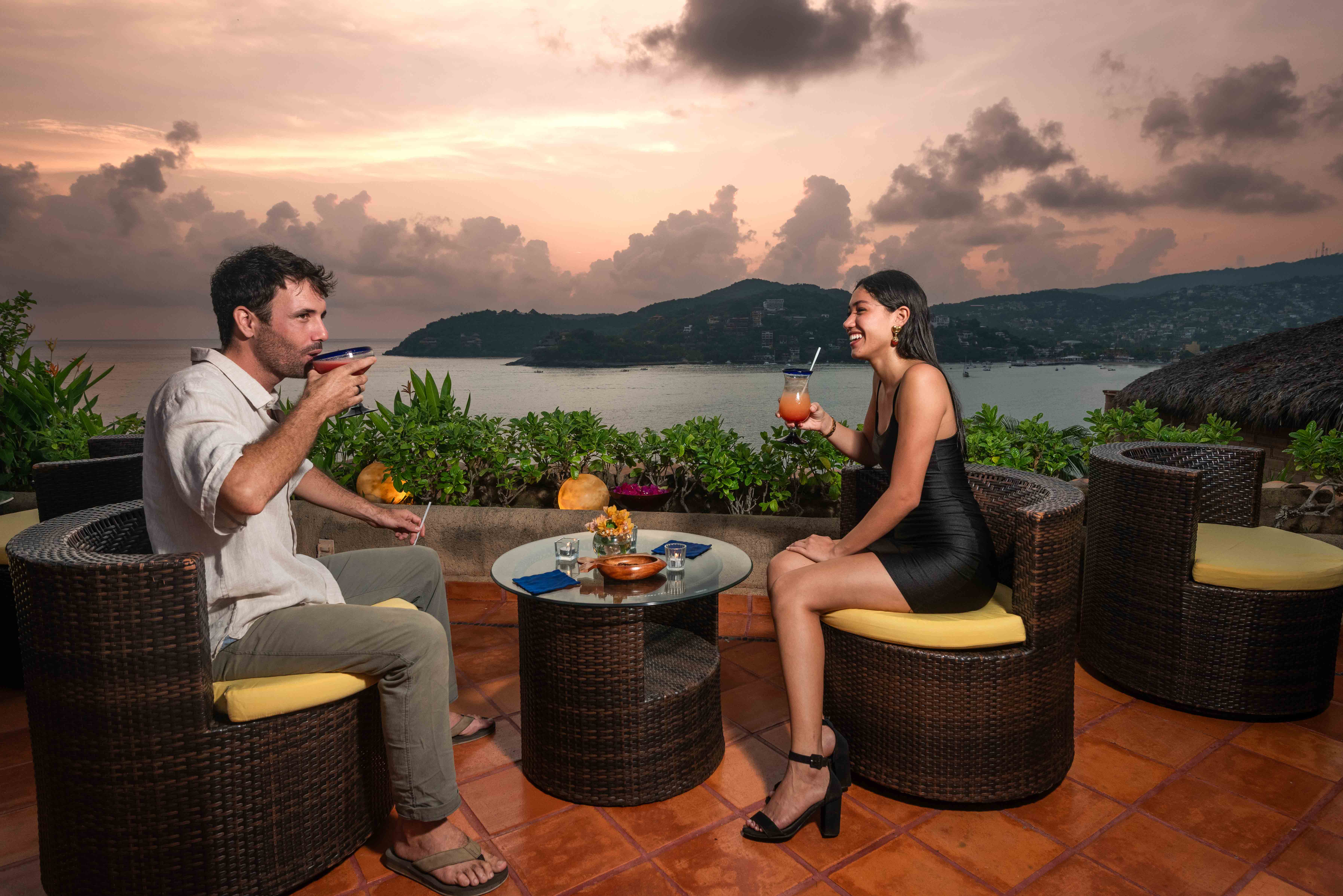 Young couple enjoying cocktails on a sunset terrace overlooking the ocean at La Casa Que Canta