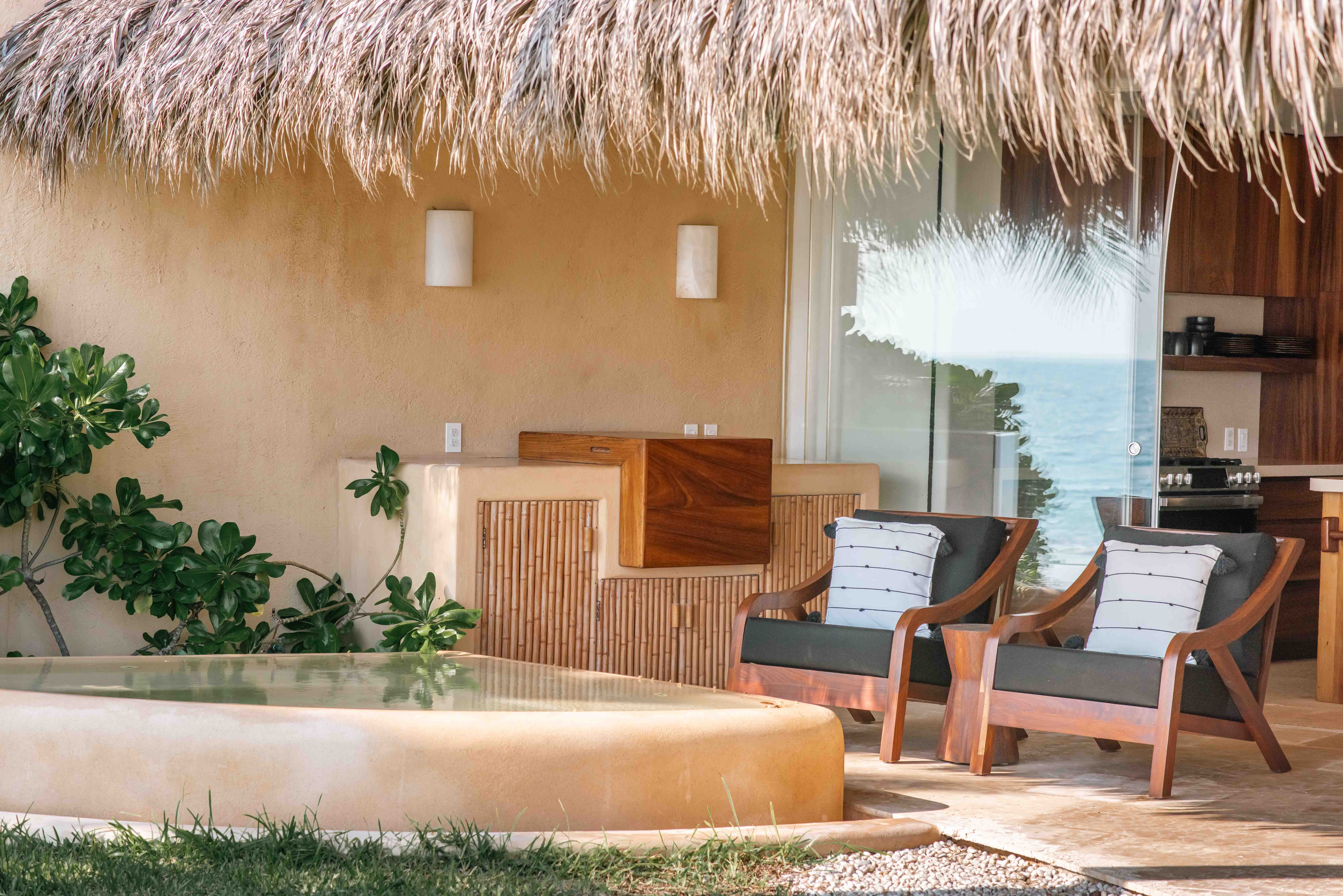 Outdoor terrace with jacuzzi, palapa, lawn, lounge chairs and kitchen in the background