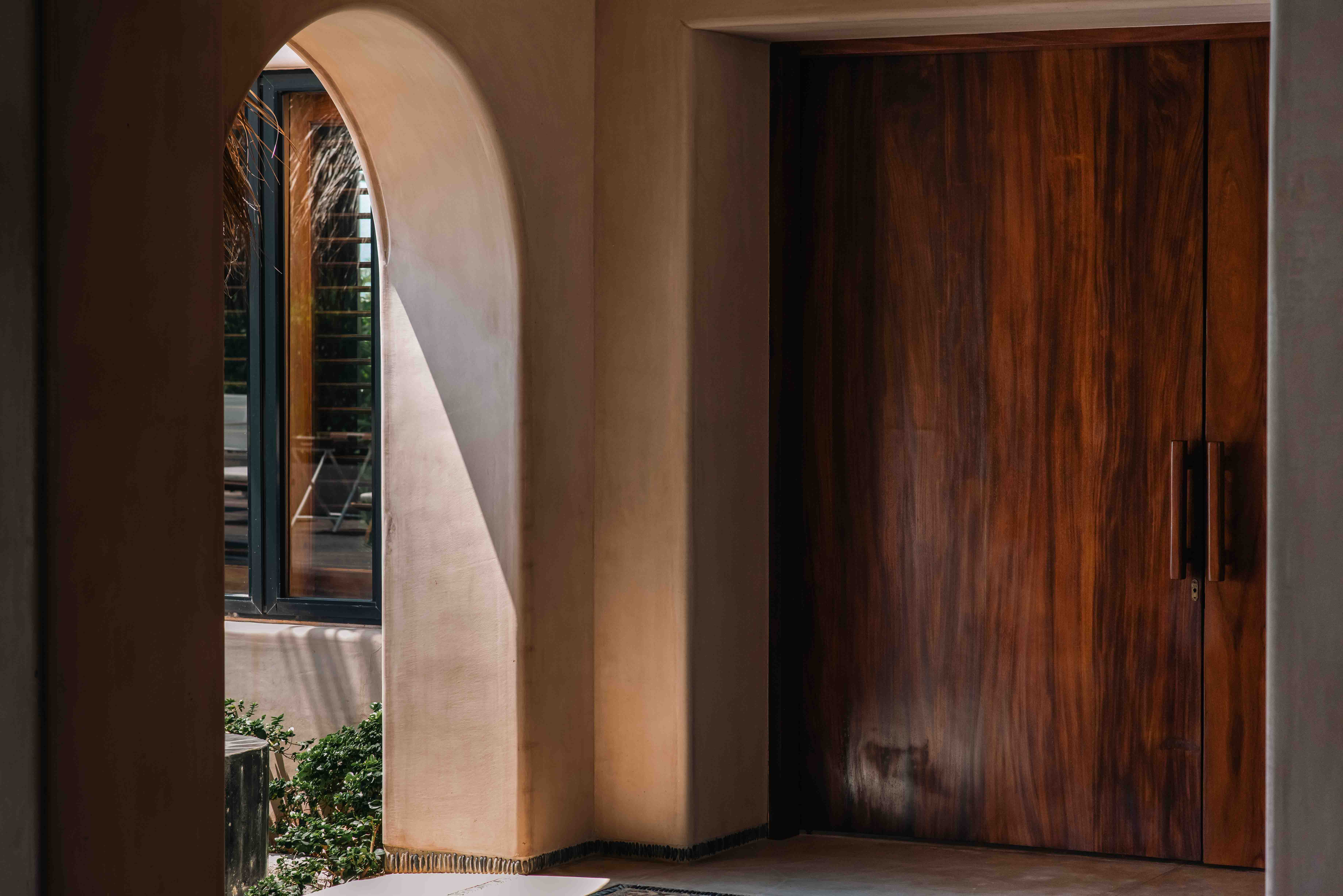 Wooden doors and curved architectural walls illuminated by natural light and shadow in a beachfront house by Zozaya Arquitectos