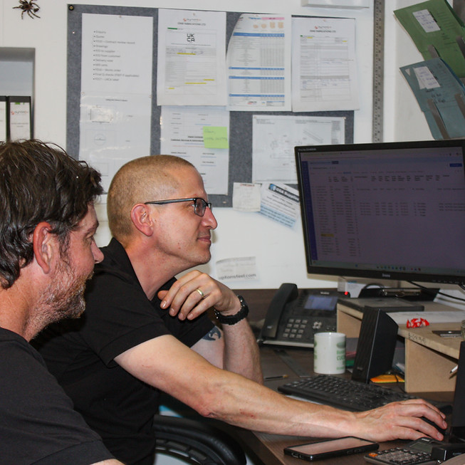 Two men in an office looking at computer screens.