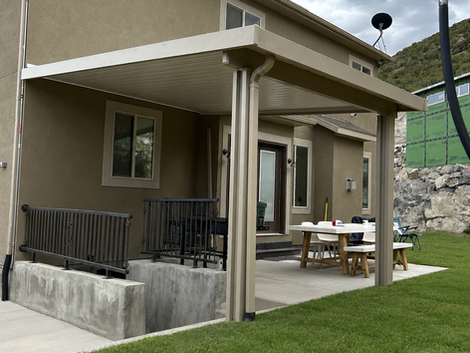 Decorative aluminum stairwell cover with square support posts protecting a basement entrance beside a backyard patio.