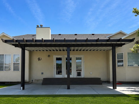 Insulated aluminum patio cover with decorative pergola-style beam ends covering a backyard concrete patio.