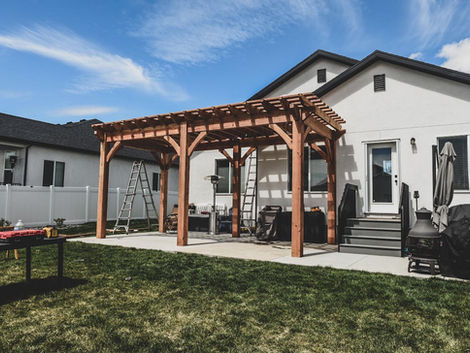 Large custom cedar pergola installed behind a home, creating a shaded outdoor seating and entertaining area.