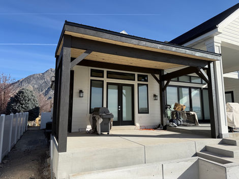 Custom heavy timber pavilion with a solid roof covering a backyard patio and outdoor seating area.