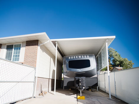 Custom aluminum RV carport with an extra-tall insulated roof protecting a recreational vehicle beside a home.