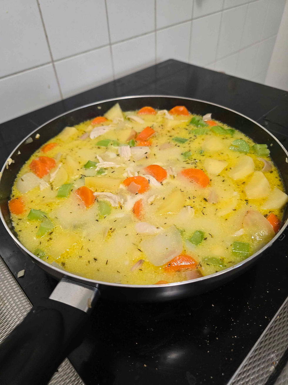 A full-to-the-brim pan of homemade soup. Clearly visible are chunks of carrot, celery, potato, onion, and strips of chicken in a yellow spiced broth.
