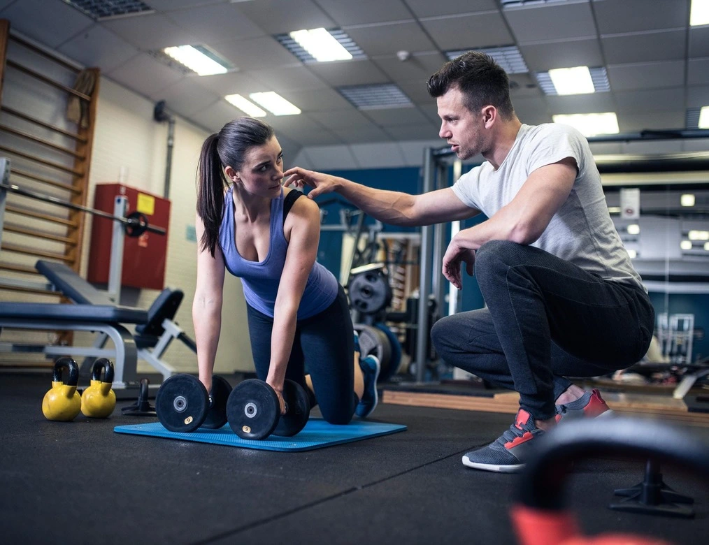 Un coach sportif passionné donnant des conseils avisés dans une salle de sport. Il explique avec assurance à une fille la pratique du fitness sans blessure. Ses gestes expressifs et ses explications détaillées captivent l'attention. Son expertise transparaît à travers son attitude bienveillante et sa posture confiante, inspirant confiance et motivation. 