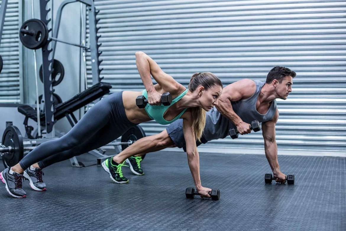 Un homme et une femme qui s'investissent pleinement dans leur séance d'entraînement avec des haltères à la salle de sport. Leur expression sérieuse témoigne de leur détermination à progresser et à atteindre leurs objectifs de fitness.