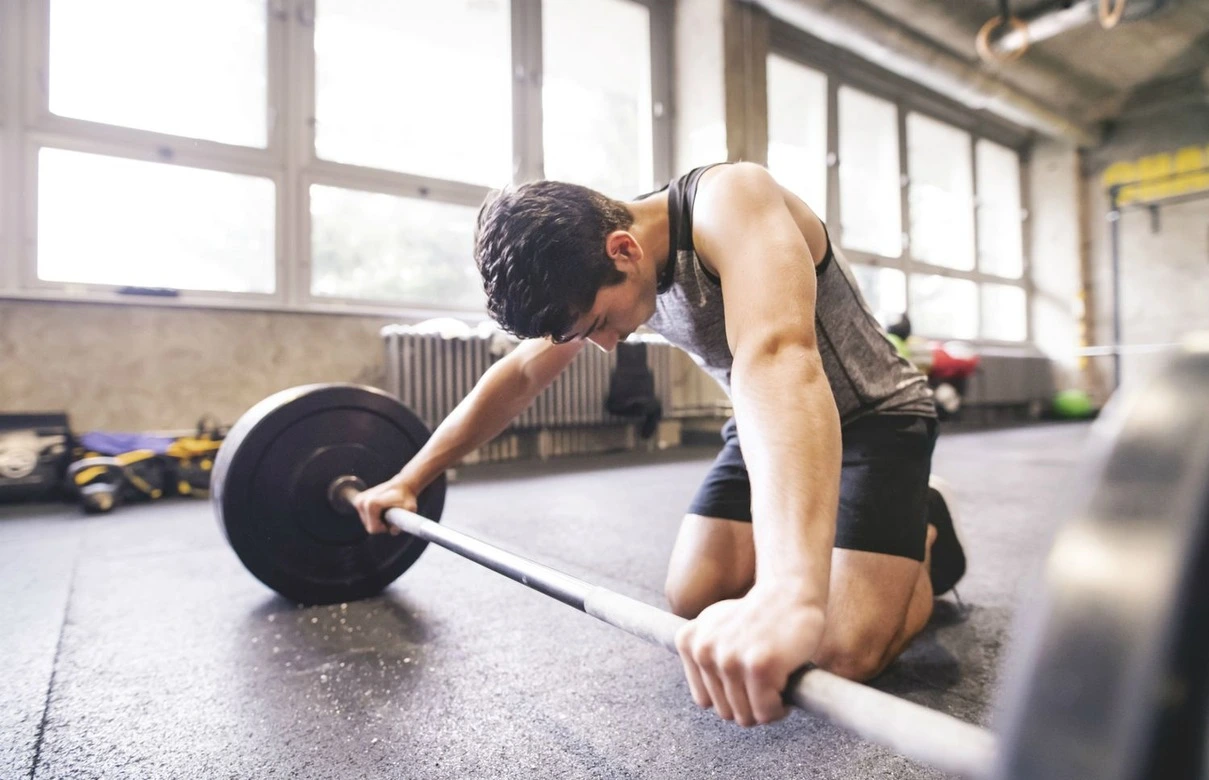 Une photo frappante mettant en scène un homme en plein entraînement dans une salle de sport, mais qui semble manquer de motivation. Son visage affiche une expression de découragement et de lassitude, tandis qu'il effectue ses exercices. Son corps semble fatigué et sa posture est légèrement affaissée.