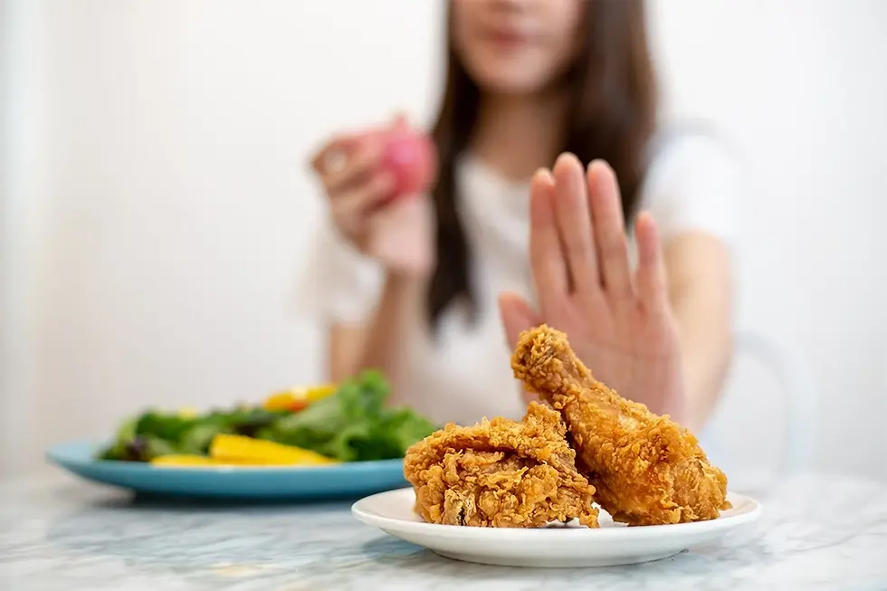 Une femme refuse les poulets frits et choisie les aliments sains sur son assiette en tenant une pomme dans sa main. Son refus déterminé de la mal bouffe met en évidence son engagement envers une alimentation saine et équilibrée pour perdre du poids plus efficacement.
