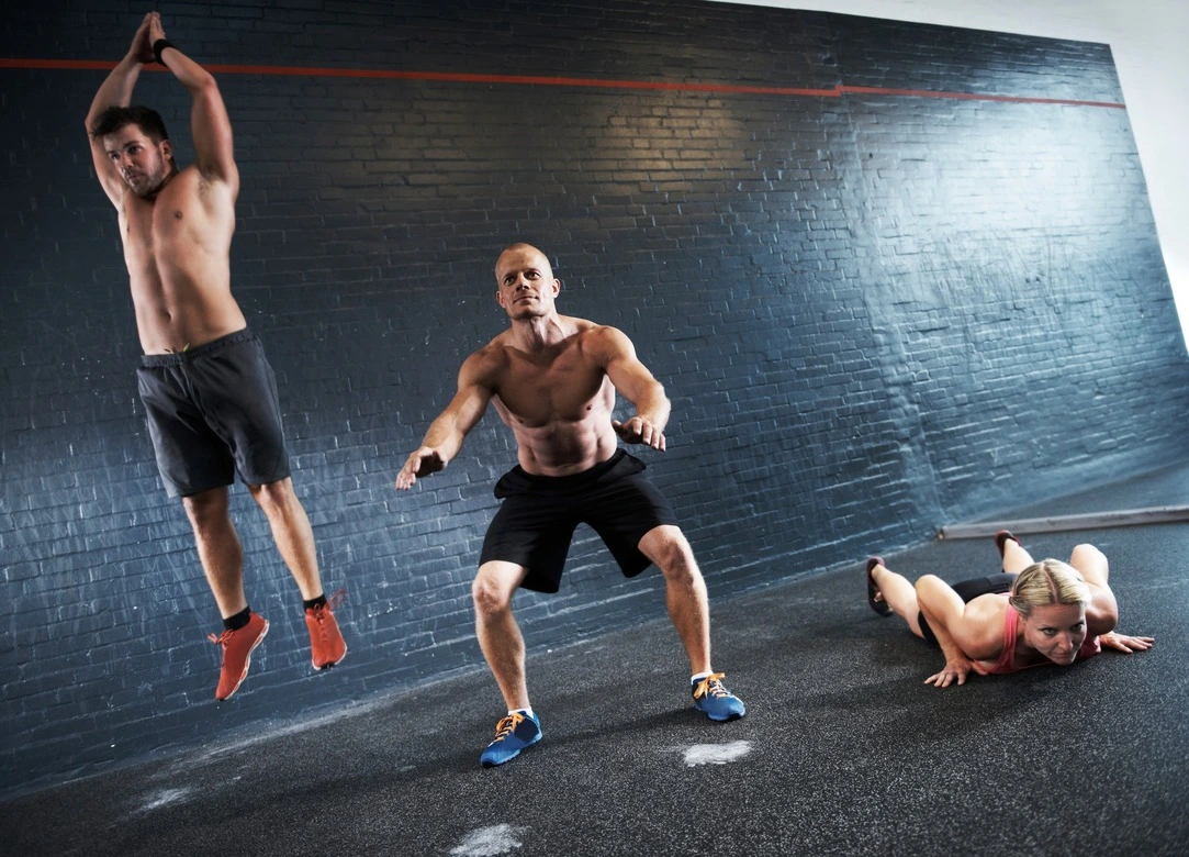 Vêtues de tenues de sport noires, trois personnes se lancent avec détermination dans une séquence exigeante de Burpee. Le premier individu effectue le saut vertical avec une puissance explosive, le deuxième se positionne en position de planche avec une stabilité impressionnante, tandis que le troisième achève la série en revenant à la position debout.