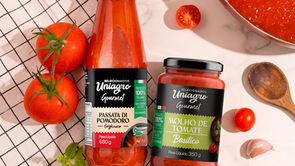 Garrafa de Passata di Pomodoro Orgânico (680g) e pote de Molho de Tomate Basílico (350g) da marca Selecionados Uniagro Gourmet, cercados por tomates frescos, alho e folhas de manjericão sobre fundo claro.