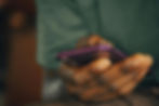 Hand holding a purple smartphone, focused on the screen. Background blurred with earthy tones, suggesting an indoor setting.