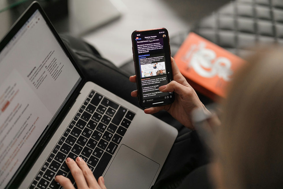 Person using a laptop with Russian text while holding a smartphone displaying a text message. Cozy setting with a blurred orange item.