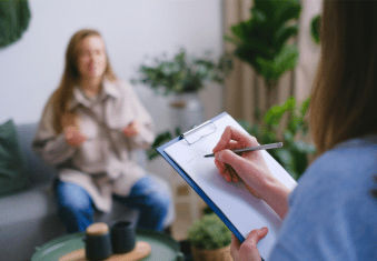 woman sitting on a couch in front of a woman writing on a clipboard