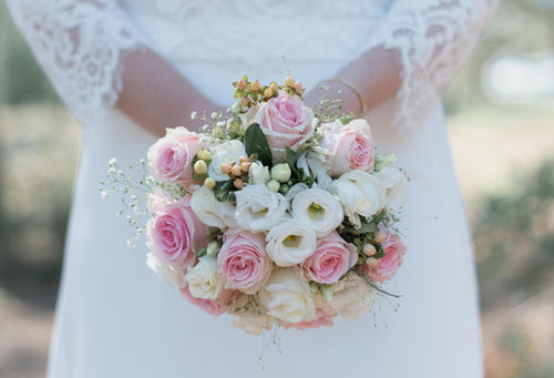 La mariee tient devant elle un bouquet de fleurs roses et blanches.