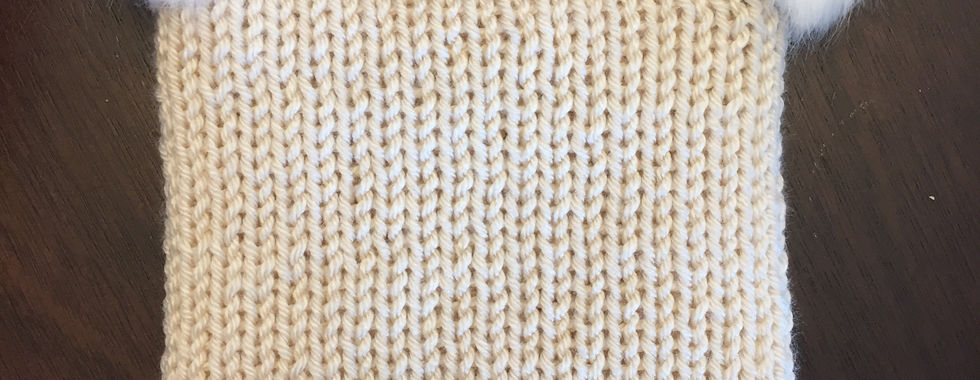 A cream hat with white pom poms on the top corners
