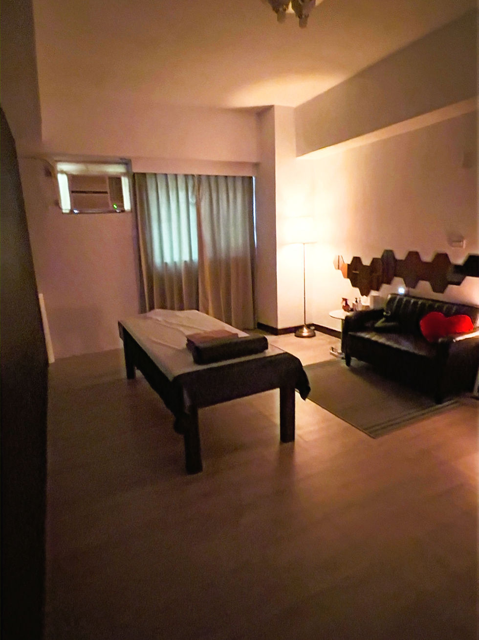 A cozy room featuring a couch, table, and lamp, designed for relaxation in a gay massage setting in