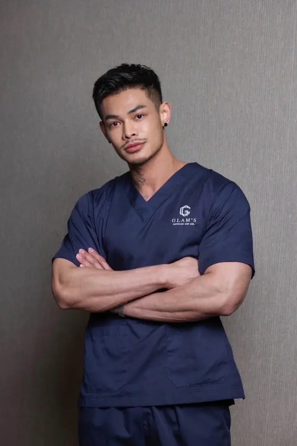  A male in scrubs stands confidently with arms crossed, exuding a professional yet relaxed vibe