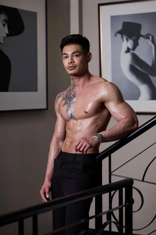 A shirtless man leans against a stairway, embodying the casual energy of a gay massage spot in Bangkok