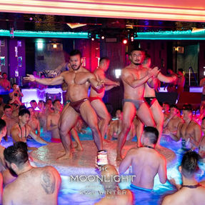 首爾同志酒吧(gay bar seoul)裡擁擠的室內泳池派對,身穿泳褲的男子在粉藍色燈光下跳舞。