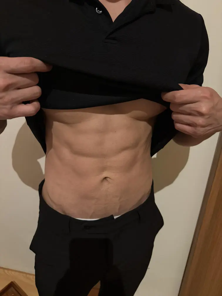 黒いシャツを着た男性が引き締まった腹筋を見せており、フィットネスと強さを強調しています。