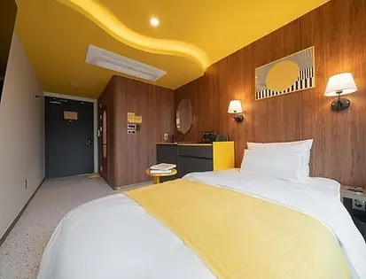Modern boutique guest room at Nouvelle Hotel Seoul Itaewon, a popular gay hotel in Seoul, featuring a vibrant yellow ceiling, wood panel walls, and a minimalist double bed.