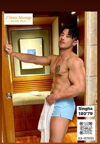 上身赤裸、短髮有紋身的男性，自信地站在曼谷gay按摩（gay massage Bangkok）水療室內，手持毛巾。房間設有木質牆板及按摩品牌標誌。