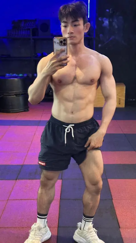 A shirtless man captures a selfie in a gym setting, emphasizing his dedication to fitness and personal health