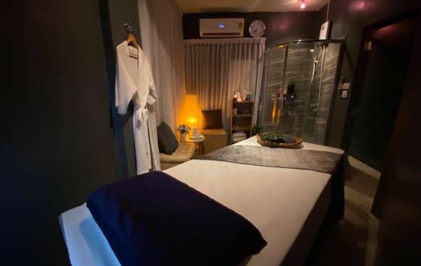 昏黃燈光下的水療室，按摩床鋪上白灰色床單。牆上掛有浴袍，柔和的燈光配搭舒適的休息區，營造出寧靜愜意的氛圍。