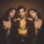 A guy is holding two bananas in his hands, and two girls are standing on each side of him.