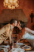 A couple kisses across a candlelit dinner table, under a chandelier. Elegant decor with golden plates and a wine bottle, creating a romantic mood.