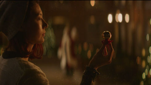 Young woman inspecting a Christmas sleigh bell in front of Santa Clause.
