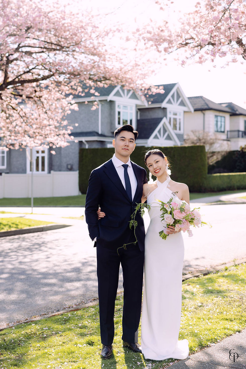 Newlyweds holding hands under blooming cherry blossom trees on a Vancouver street during their spring wedding day.