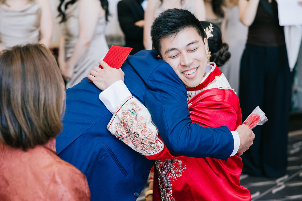 Groom in red Cantonese wedding attire hugging a family member with a red envelope at the banquet