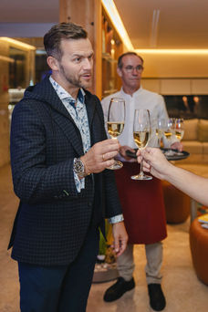 Homem elegante é recebido com um copo de espumante durante evento em restaurante de luxo