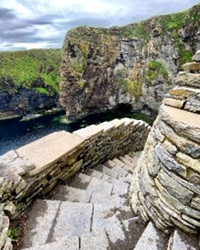 The historic Whaligoe Steps winding down a rugged Scottish cliff to a hidden harbour, surrounded by dramatic coastal views and wild sea cliffs