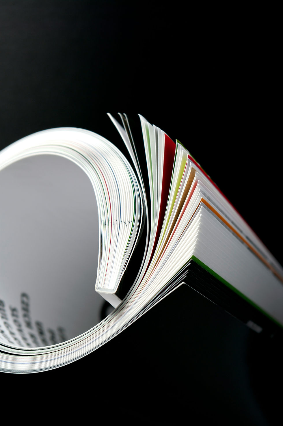 An open magazine with pages fanned out, showing colourful printed edges against a black background.