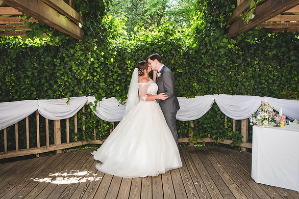 Bride and groom kissing on a wooden deck in front of an ivy-covered wall — Jon Snapaway Photography.