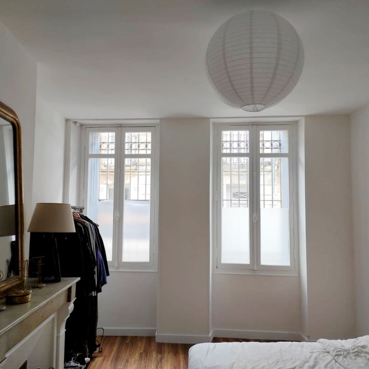 Fenêtres d'une chambre dans un appartement ancien, peintes en bmanc, murs blancs. Cheminée ancienne en marbre ornée d'un miroir ancien doré.