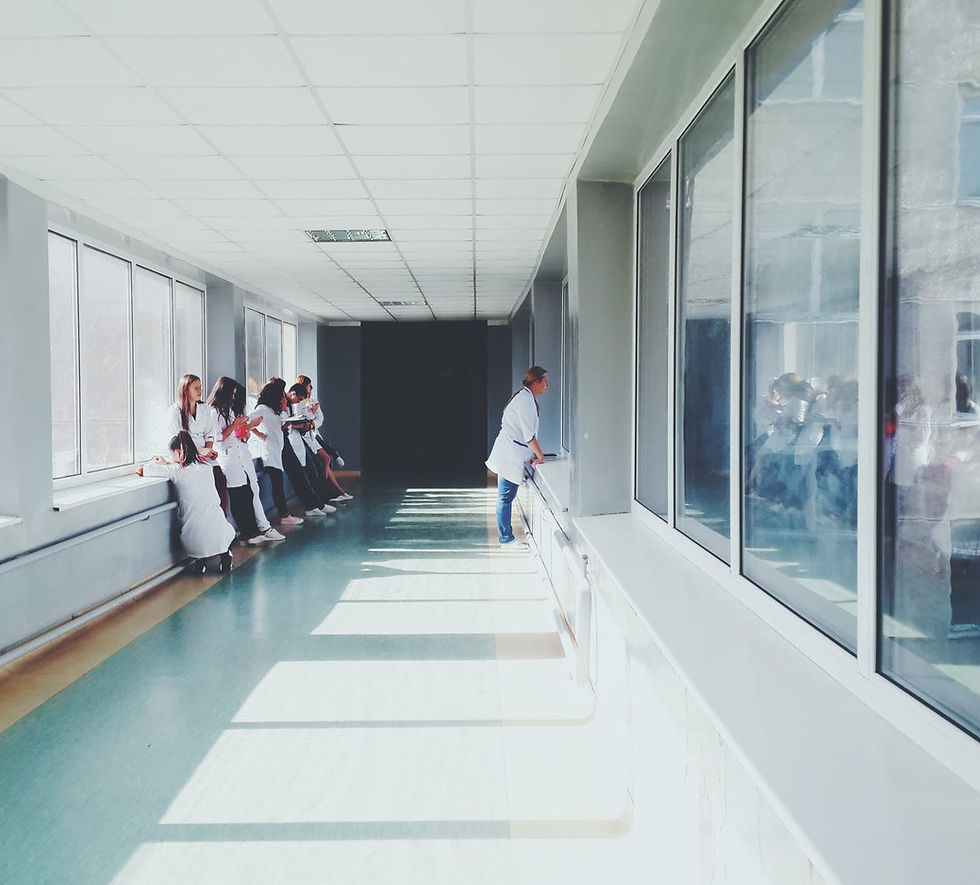 long hallway with white ceiling, walls and linoleum floor, a number of young people in white coats looking out a window