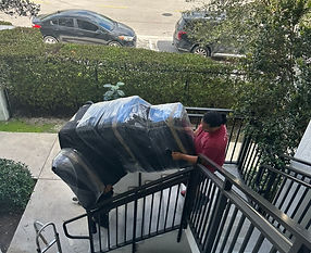 Two men carrying a couch that is wrapped in black plastic, down stairs. 