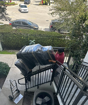 Two men carrying a couch that is wrapped in black plastic, down stairs.