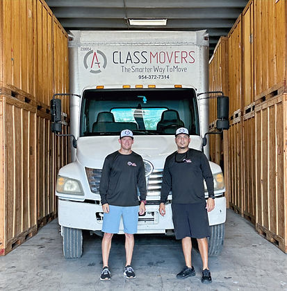 Two men in front of a moving truck inside of a warehouse. Wooden storage vaults are in the backgrund.