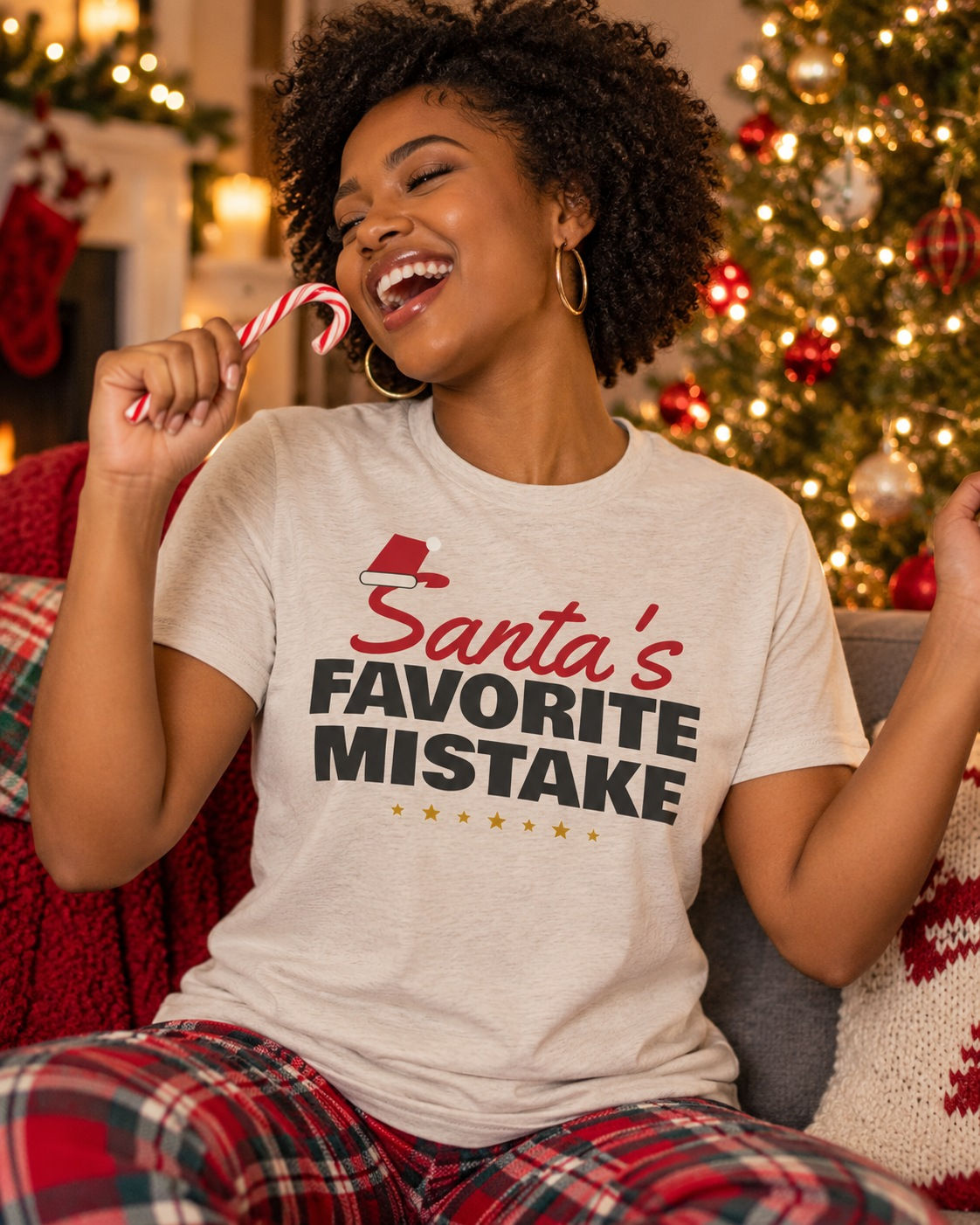 Laughing woman holding a candy cane by a Christmas tree, wearing the Santa's Favorite Mistake funny Christmas t-shirt
