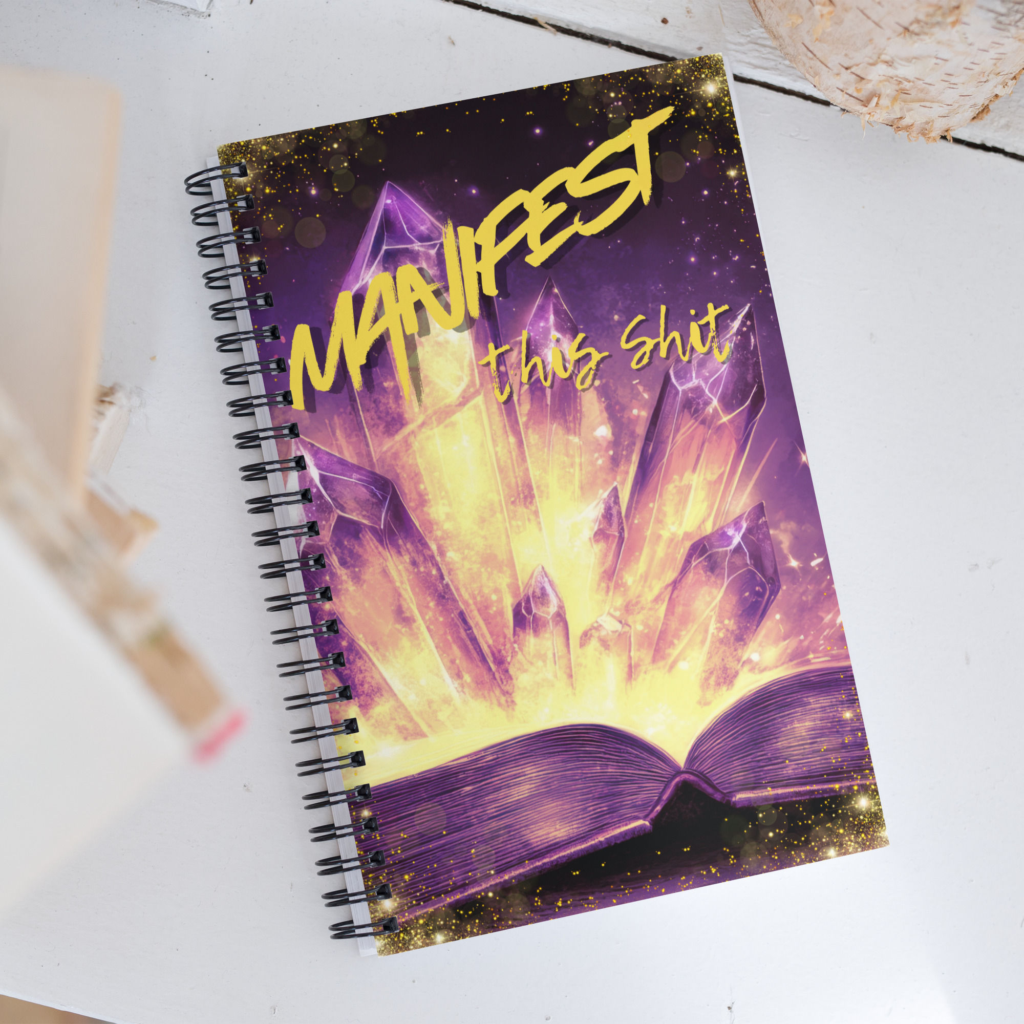 Spiral notebook-cover designed with crystals jutting from a book and the saying "Manifest this shit"