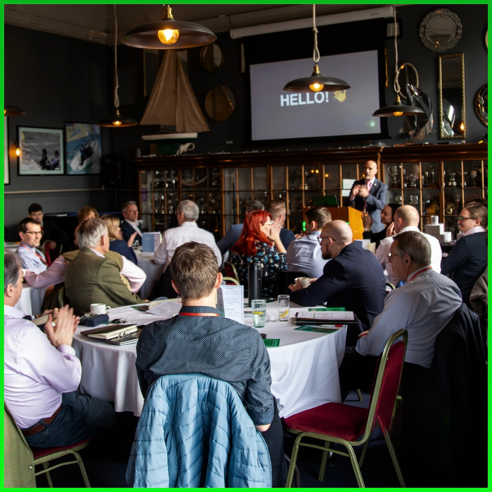 Photo taken at the summit. Steve is talking while the audience is sat at tables. 