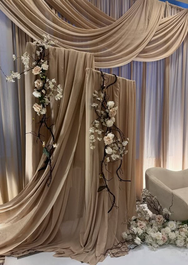 Beige draped event backdrop with white floral vines and a cream chair, creating a soft, romantic wedding display