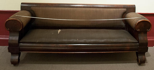Long sofa with dirty and tattered upholstery.